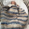 blue and tan striped baby blanket on a sleeping baby in a crib