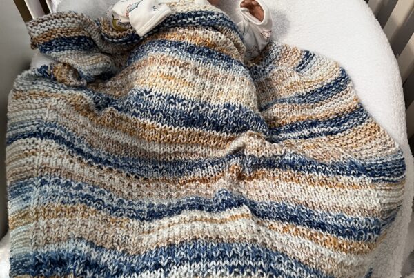 blue and tan striped baby blanket on a sleeping baby in a crib