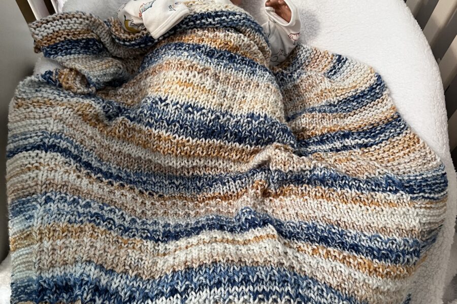 blue and tan striped baby blanket on a sleeping baby in a crib