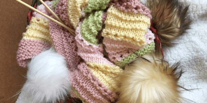 pastel baby blanket with pompoms and knitting needles